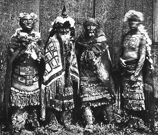 Early photo showing Masset shaman with man on right showing tattoos of the Bear on chest and a Whale on his forearm.